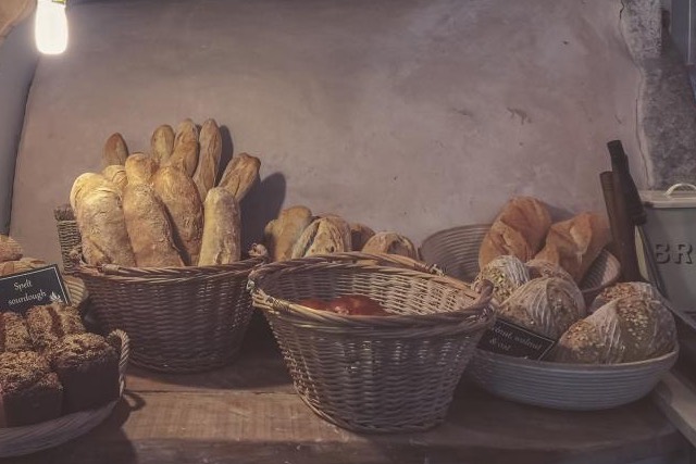 Baskets of fresh loaves on a wooden counter in front of a bakery's oven