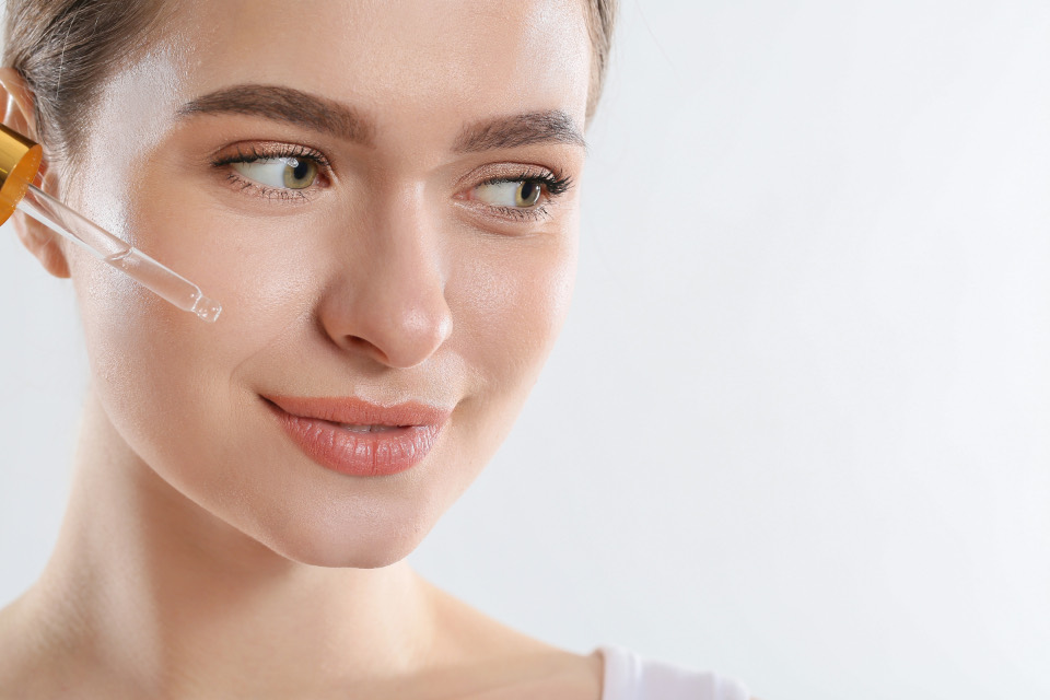 Woman with clear, glowing skin holding a serum dropper near her cheek