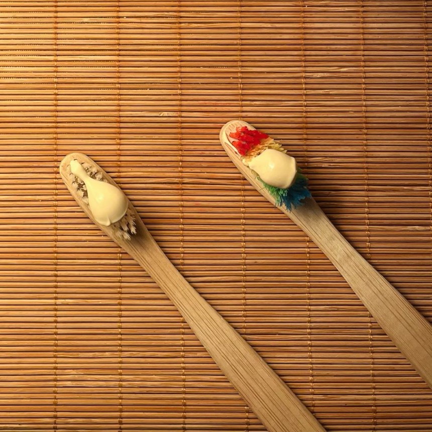 Two bamboo toothbrushes with toothpaste on a bamboo mat