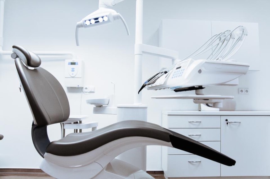 A bright treatment room with a reclining chair, an overhead light and white cabinets