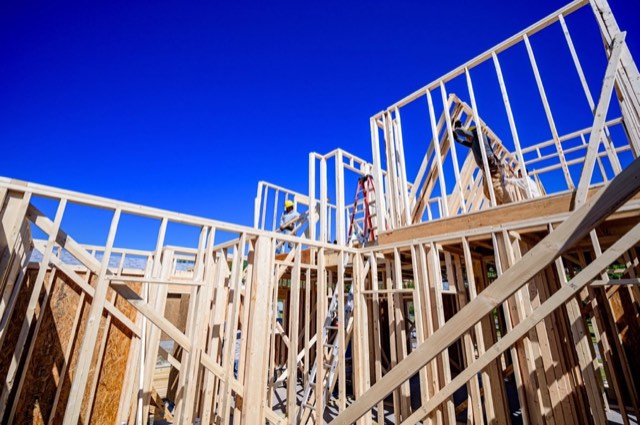 New wood framing for a two-storey addition against a blue sky, with two carpenters working on the upper floor