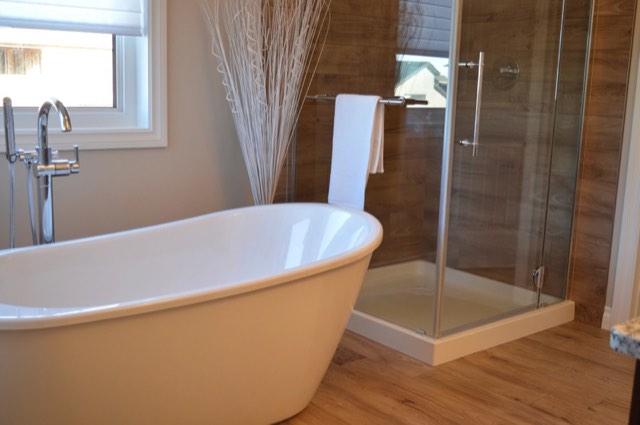 Bathroom with a white freestanding tub and floor-mounted faucet beside a glass shower with wood-look tile