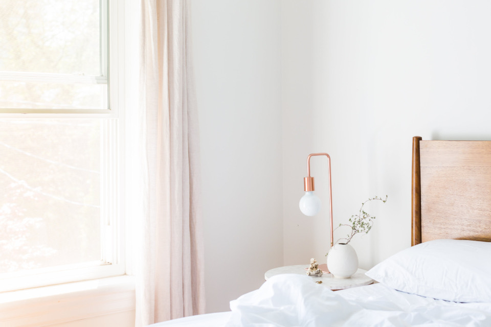 A bright bedroom with a freshly made white bed and a bedside lamp