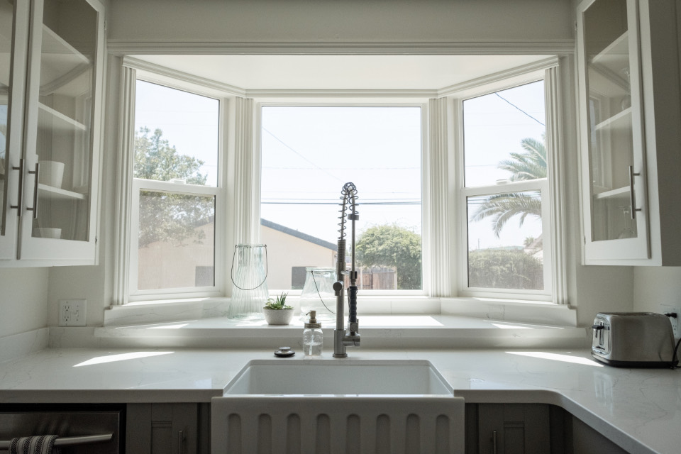 A bright white kitchen with clear counters and a farmhouse sink under a bay window