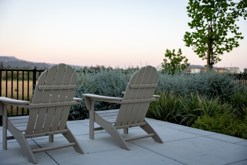 Two Adirondack chairs on a pale paver terrace at dusk, facing a border of silver shrubs and grasses with hills beyond