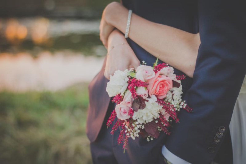 A bride's arms around the groom, holding pink and white roses