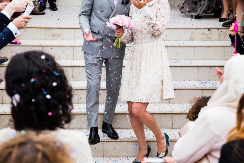 Guests throwing confetti as a couple walks down stone steps