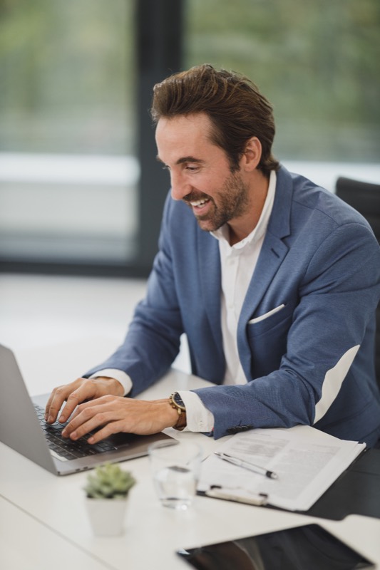 Thomas Brannock, smiling, in a blue blazer at his desk with a laptop.