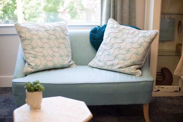 Pale blue linen loveseat with two patterned cushions beside a small white marble table holding a succulent