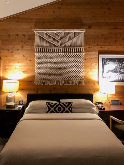 Bedroom with a cedar plank wall, a large macramé hanging above the bed and two glowing table lamps
