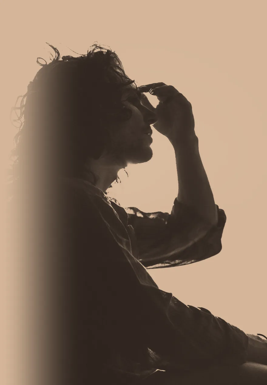 Silhouette of a person pressing a hand to their forehead against a warm evening sky