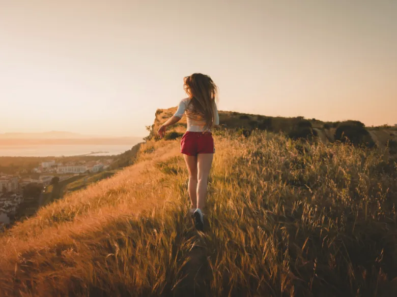 A woman running along a grassy ridge above the sea at sunset