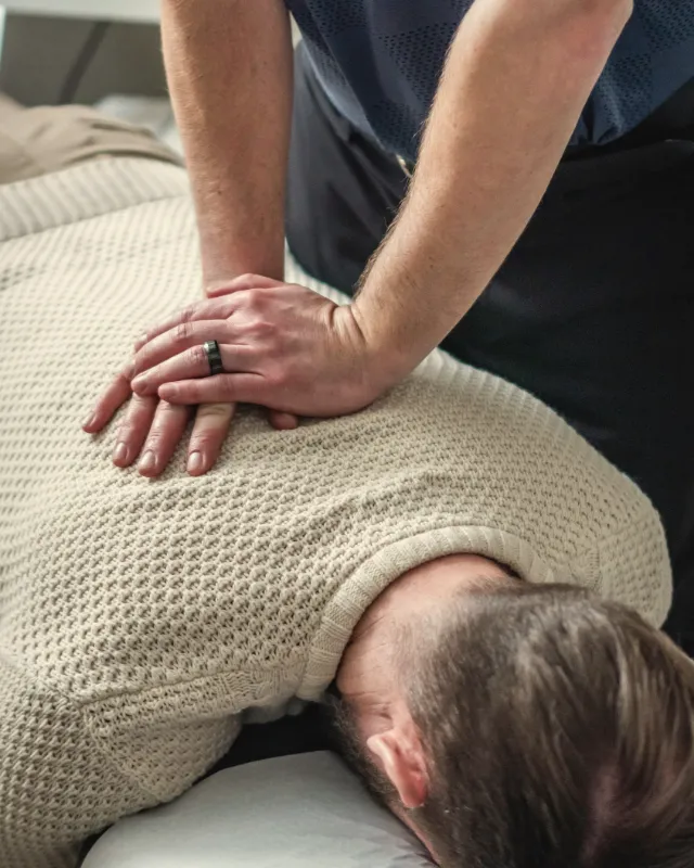 A chiropractor's stacked hands adjusting the upper back of a man lying face down on a padded table