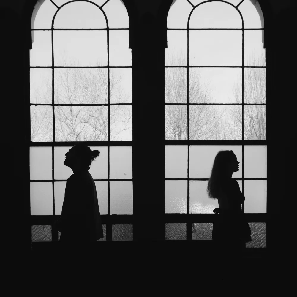 Two people in silhouette, each at a tall arched window