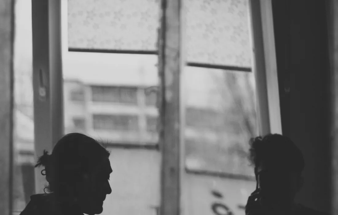 Two people in silhouette talking across a table by a window