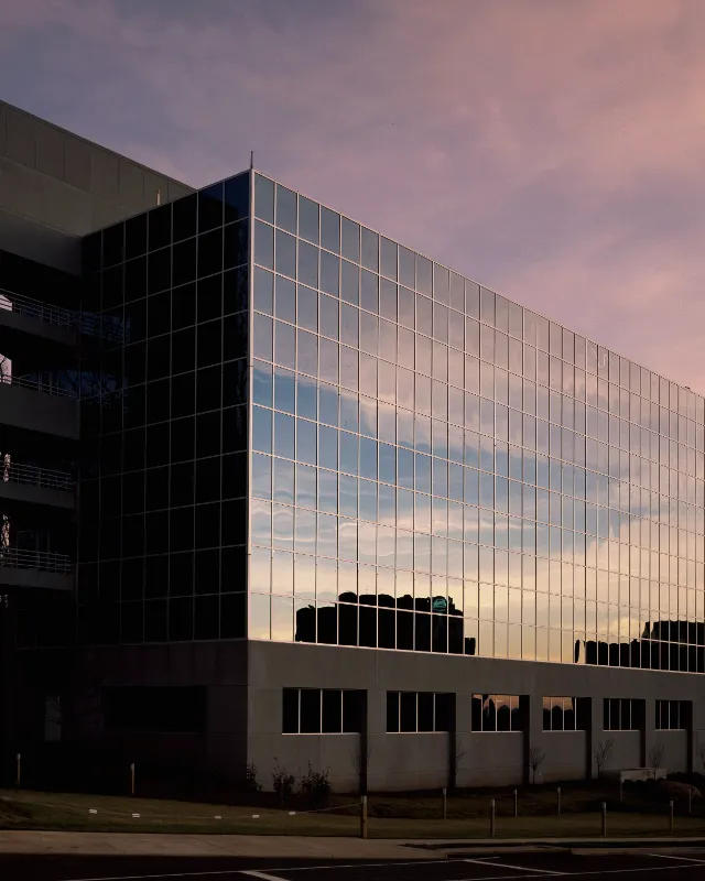 A glass office building at dusk, its curtain wall reflecting a pink sky.
