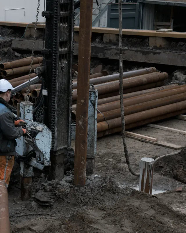 Steel foundation piles stacked beside a drilling rig on a muddy site.