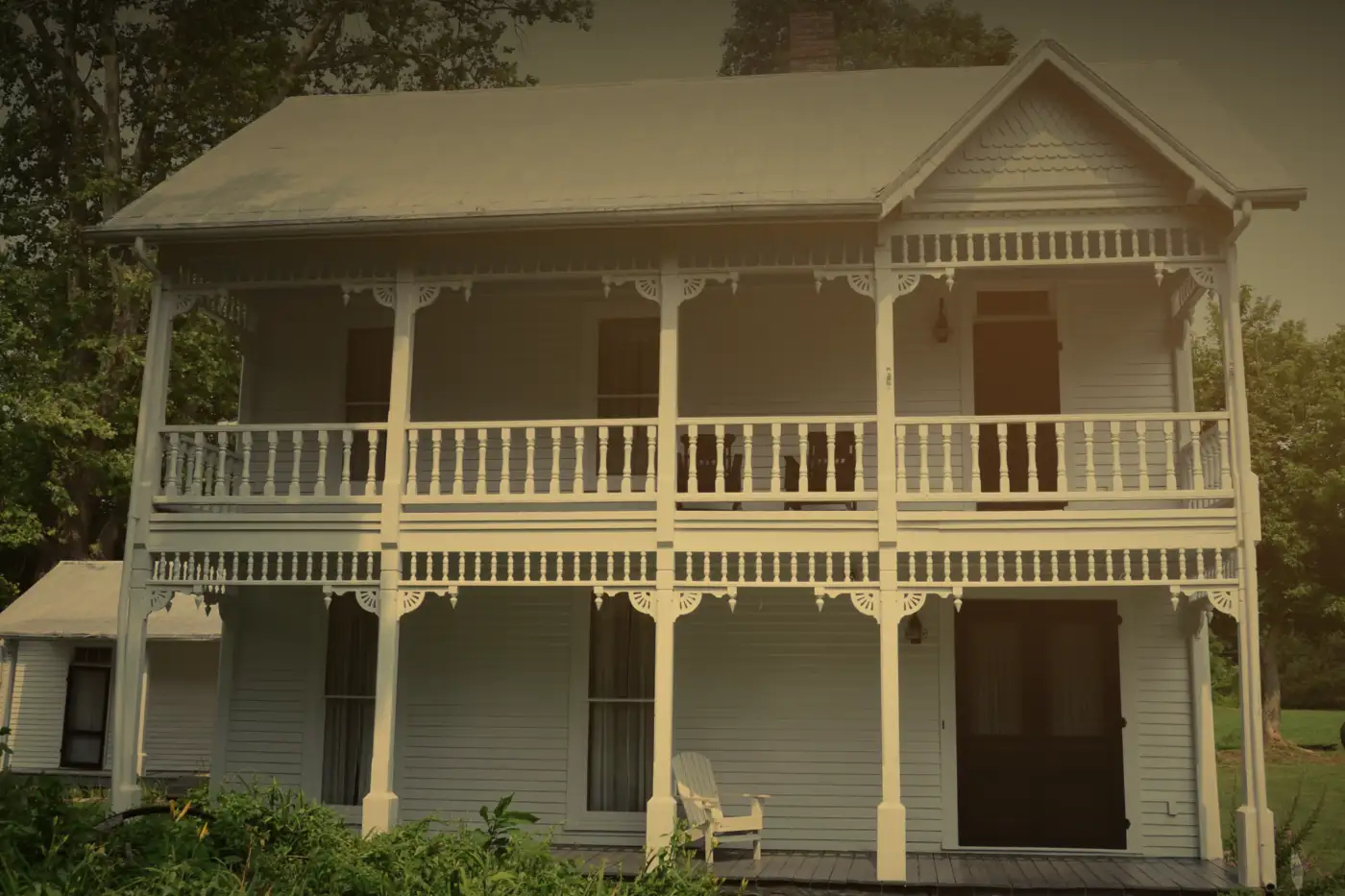 A white two-story house with a covered porch on both floors, in late-afternoon light.