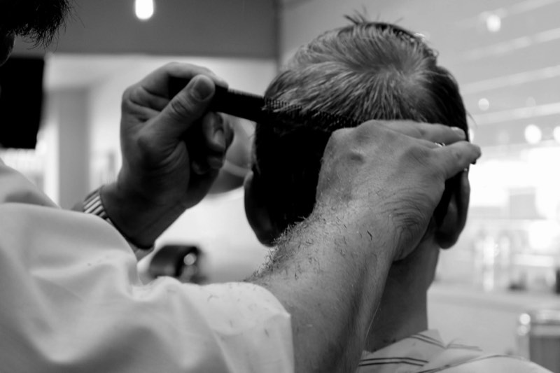 Gil running clippers up the back of a client's head, in black and white