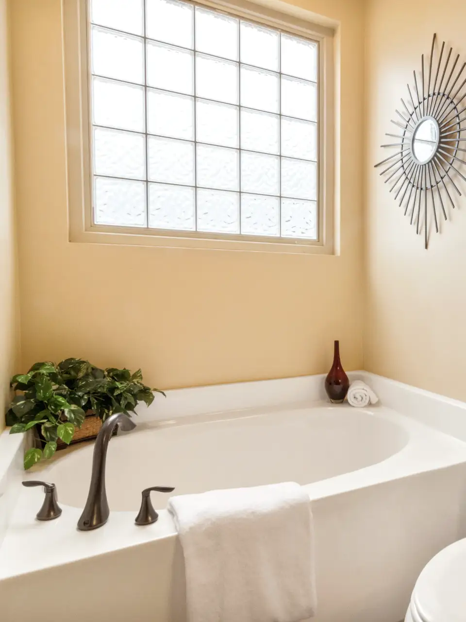 Sample before: a 1990s bathroom with a white corner tub, glass-block window and a sunburst mirror on peach walls.