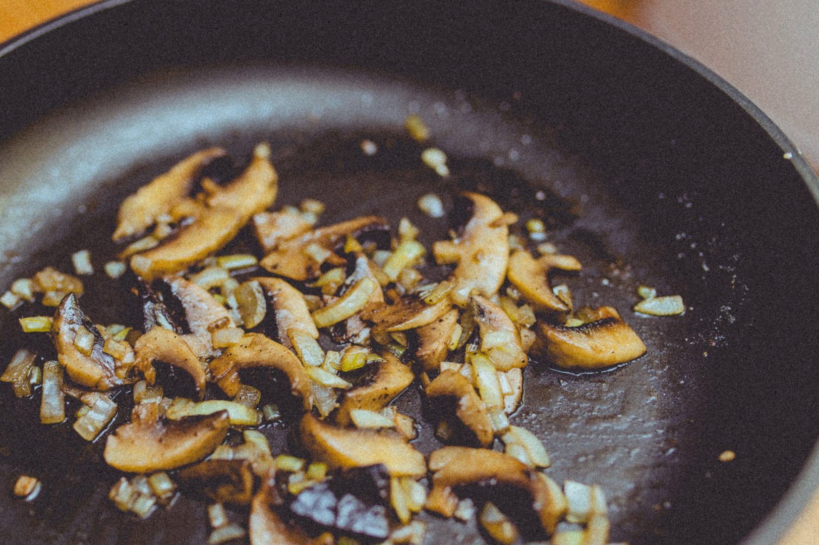 Sliced mushrooms and diced onion browning in a dark cast-iron pan.