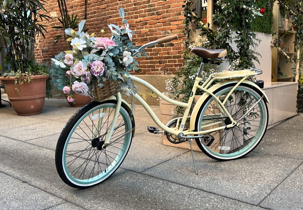 A cream beach cruiser with mint tires and a basket of flowers parked on a city sidewalk