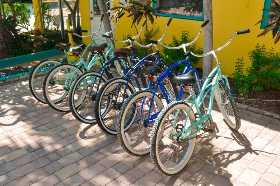 A row of aqua and blue beach cruisers parked on a sunny brick patio