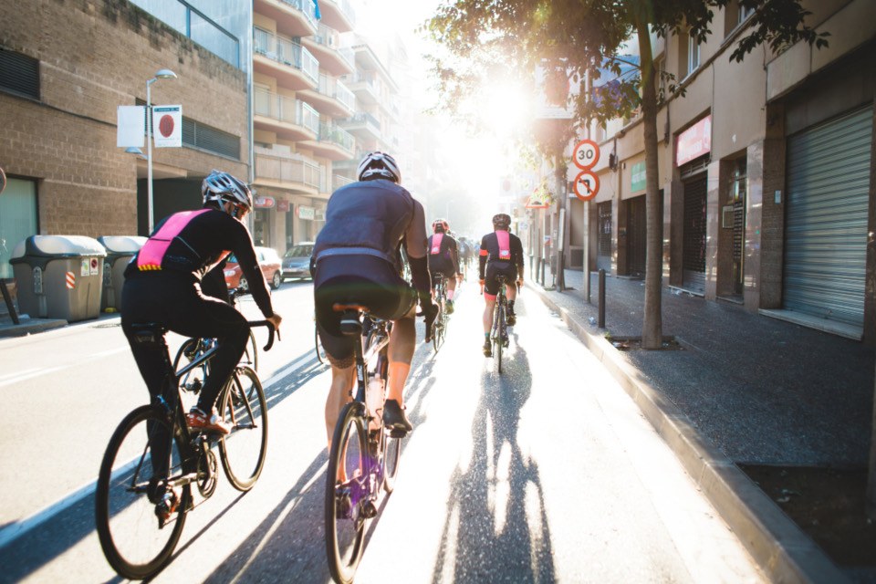 A group of cyclists riding away down a sunny city street
