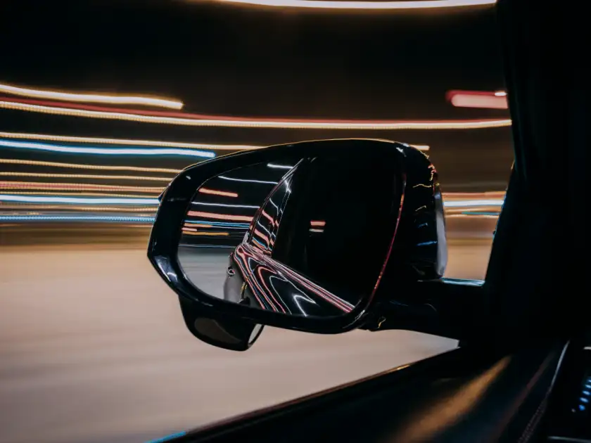 A side mirror on a moving car, city light streaking past