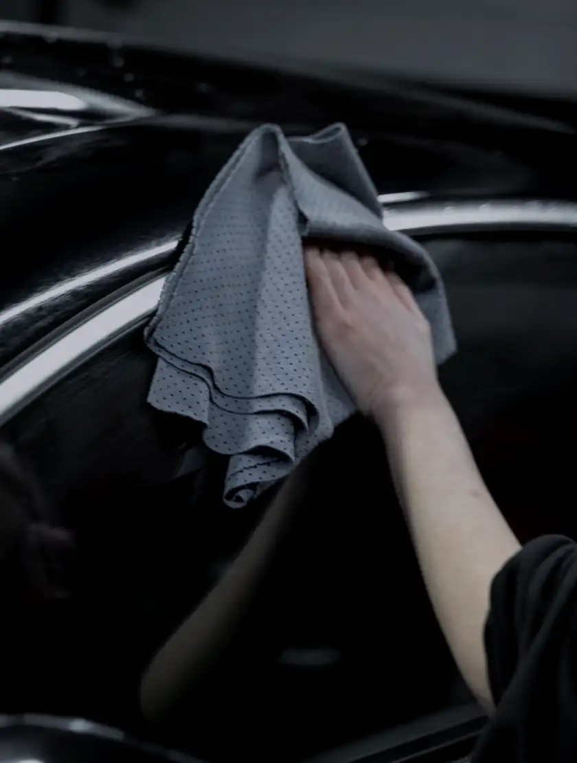 A detailer wiping deep, corrected black paint with a soft grey towel
