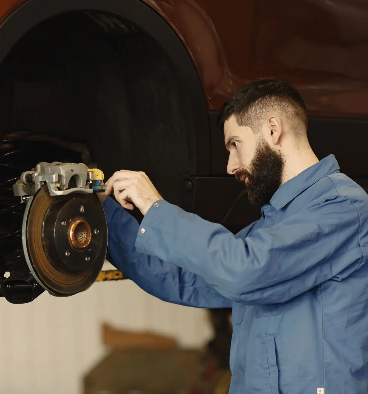 A technician checks the brake caliper and rotor on a car raised on the lift.