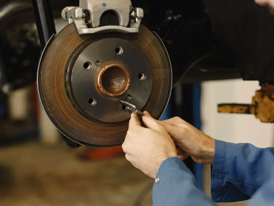 Gloved hands check a brake rotor and caliper with the wheel off.