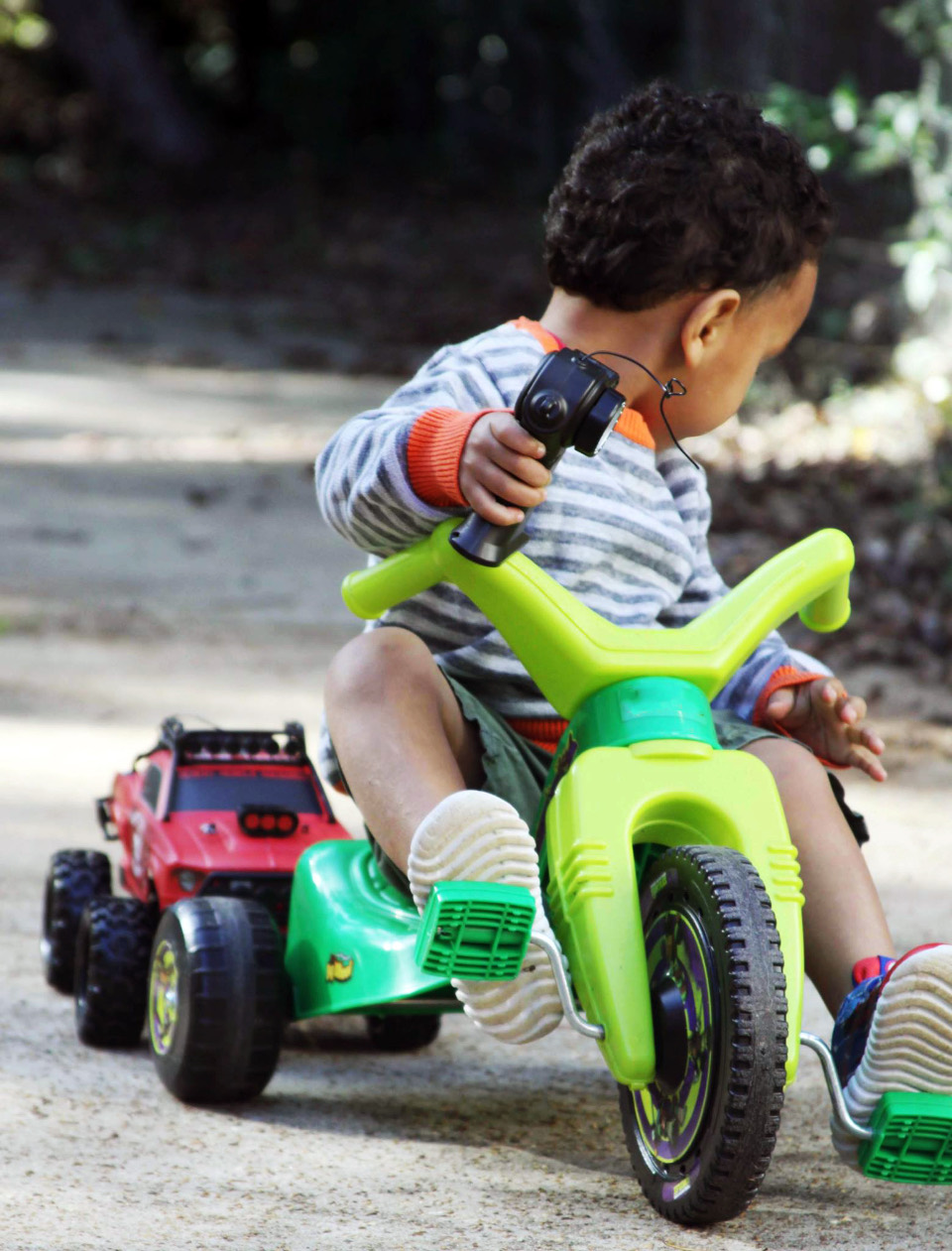 A toddler rides a green tricycle on a paved path.