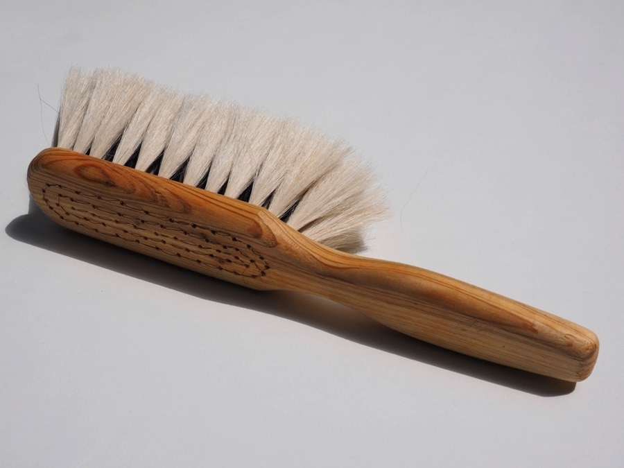 Soft goat-hair dusting brush with a wooden handle on a pale grey surface