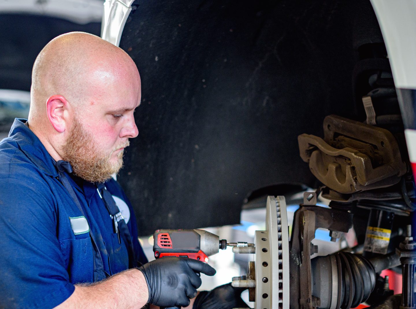 A technician fitting new front brake parts on a car raised on a lift