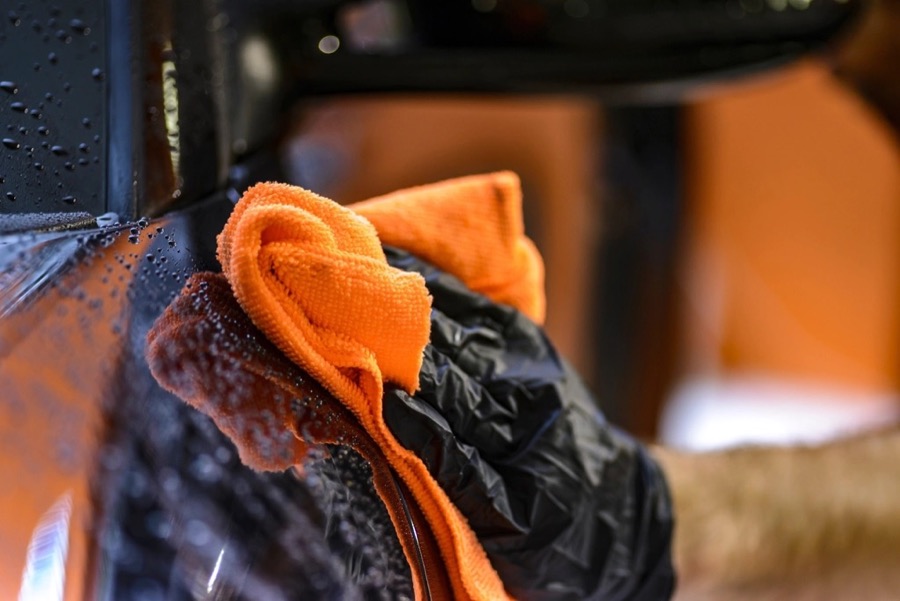 An orange microfiber towel drying a dark, beaded car panel