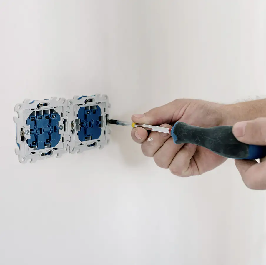 An electrician tightens a new outlet into a white wall with a screwdriver, in black and white.