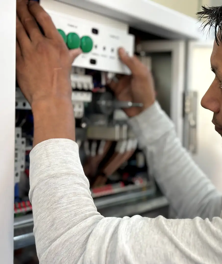 An electrician reaches into an open breaker panel to seat a breaker, in black and white.