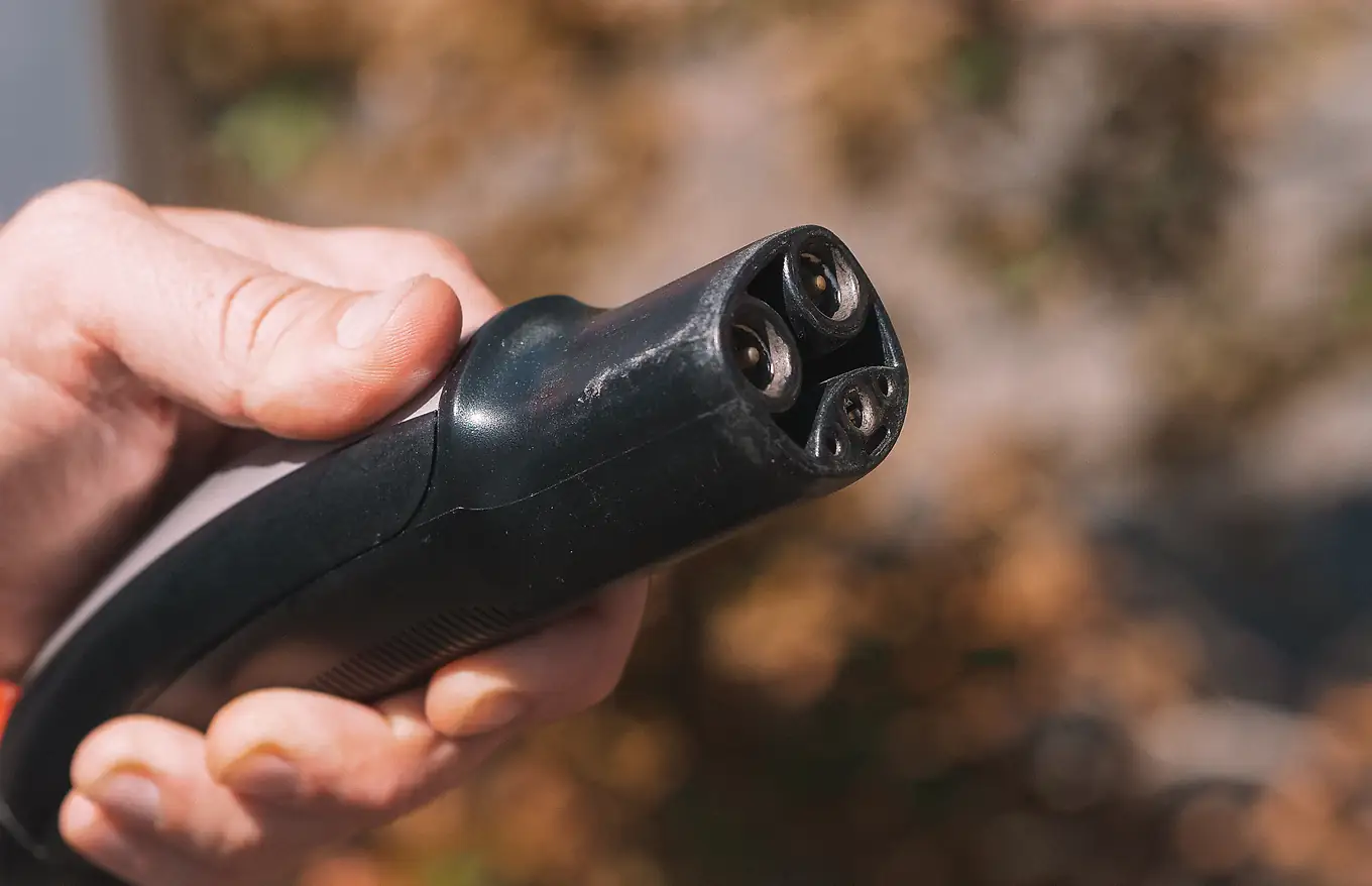 A hand holds an EV charging connector, ready to plug in.