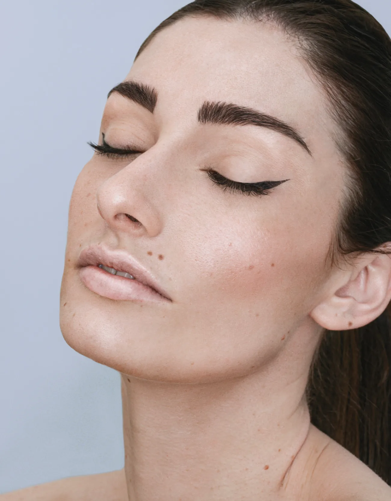 A woman with her eyes closed and chin lifted, calm, against a pale blue wall
