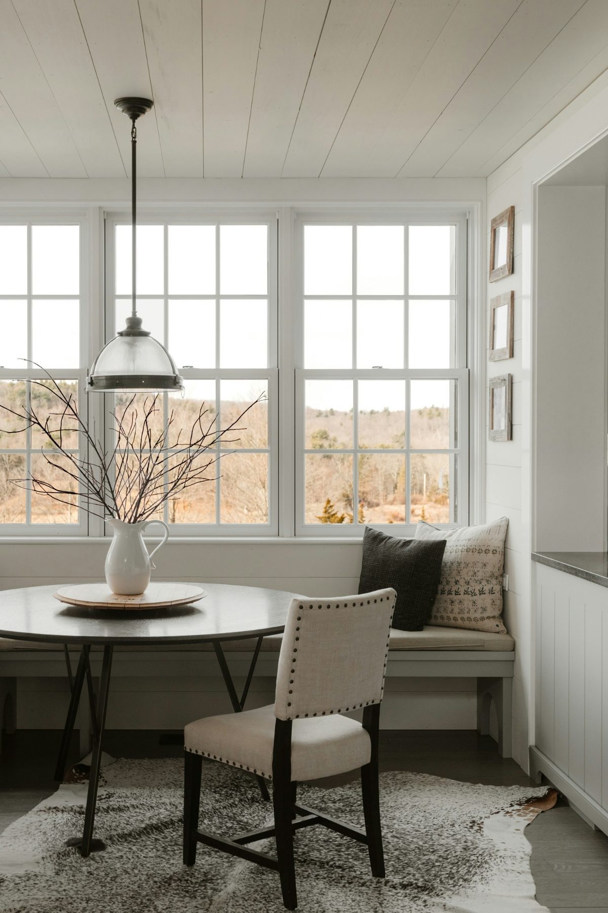 Bright white-paneled kitchen opening onto a dining nook with a glass pendant light and a table under a large window