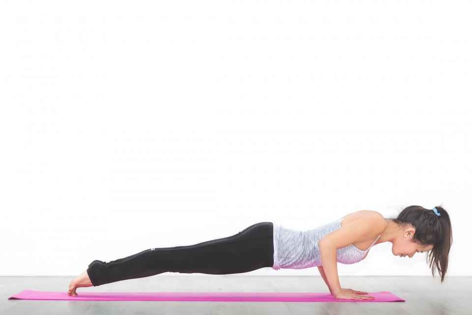 A student holding a plank on a pink mat in a white room