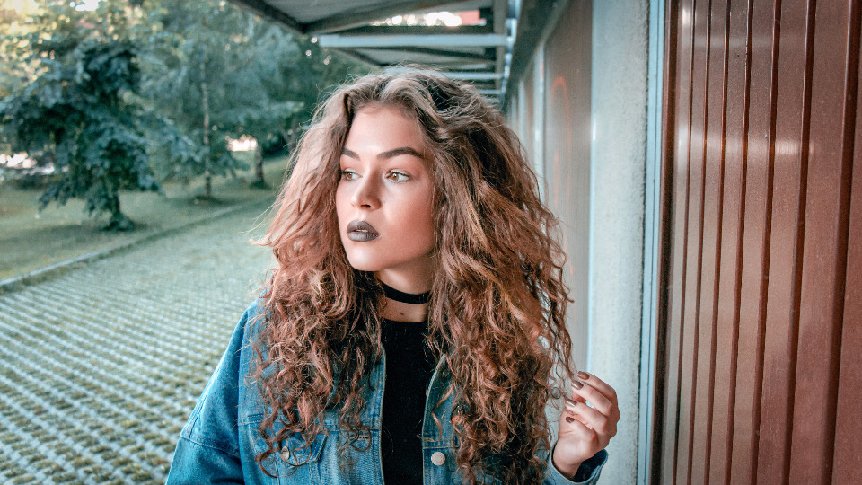 Woman with long, defined auburn curls and a denim jacket