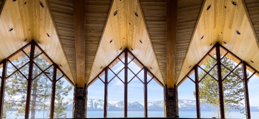 Hall interior with a pine ceiling folded into three gables above tall windows that look out to water and snowy mountains
