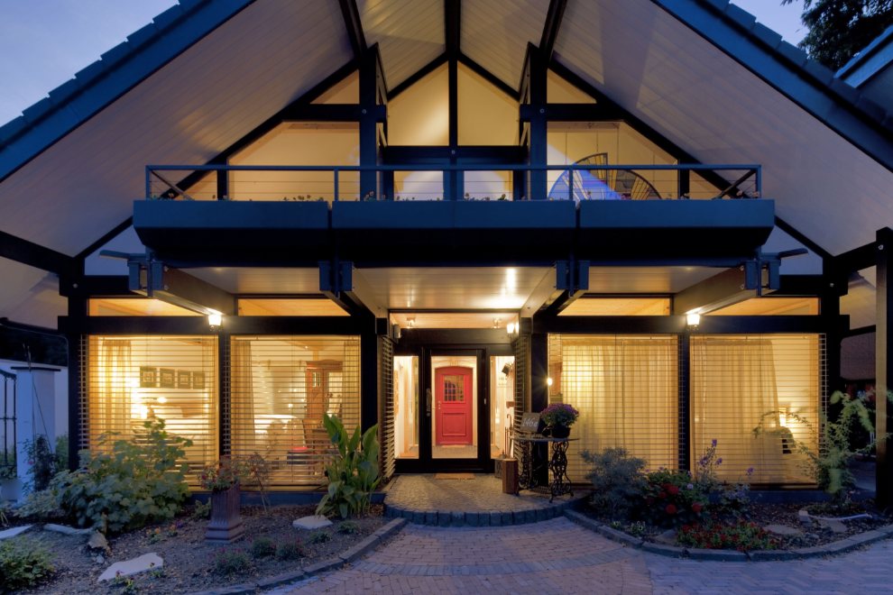 Timber-frame house with a tall glass gable, lit from inside at dusk, with a red front door
