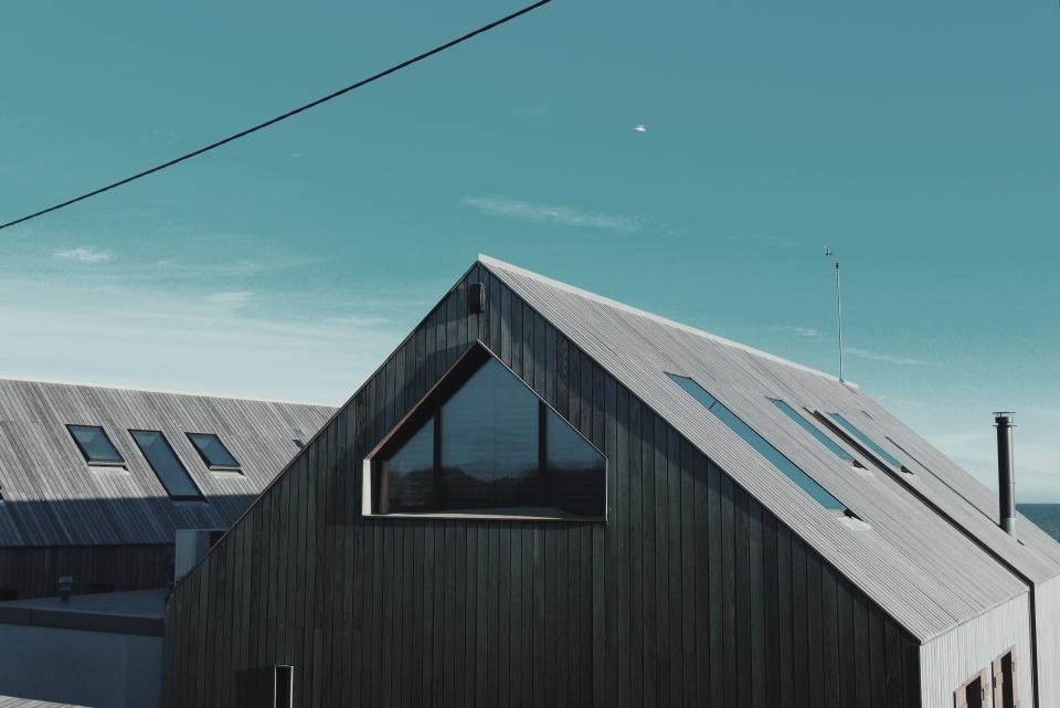 A modern dark house with a steep metal roof and skylights.